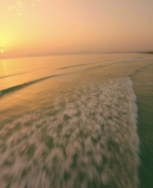 FPV drone skimming the surf along a beach at sunset
